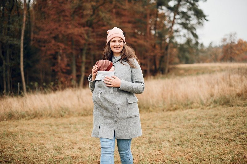 Eine Frau in einem grauen Mantel hält ein Baby in einer Tragevorrichtung